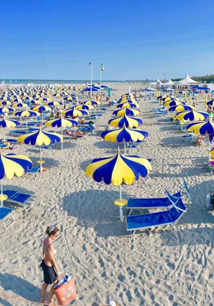 Überfüllter Strand mit gelb-blauen Sonnenschirmen, ruhiges Meer.