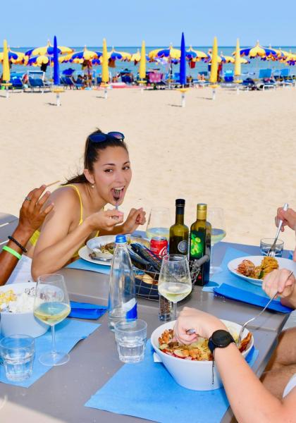 Amici che pranzano in spiaggia sotto ombrelloni colorati.