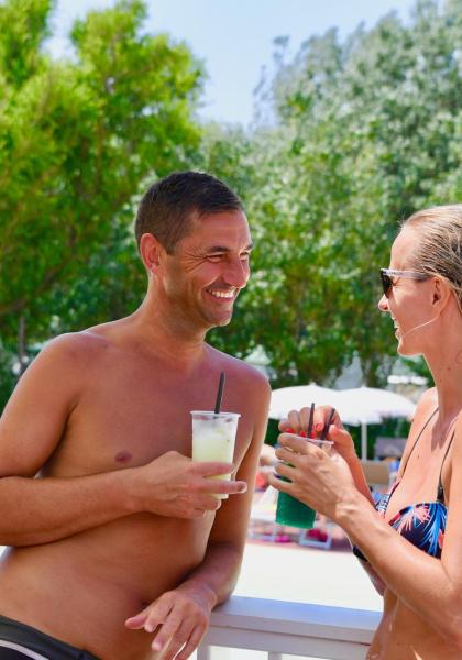 Zwei lächelnde Personen mit Cocktails am Pool.