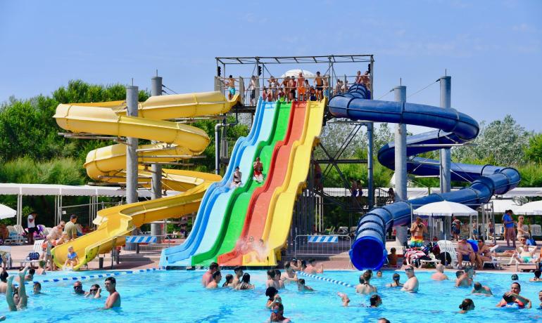 Parco acquatico con scivoli colorati e piscina affollata.