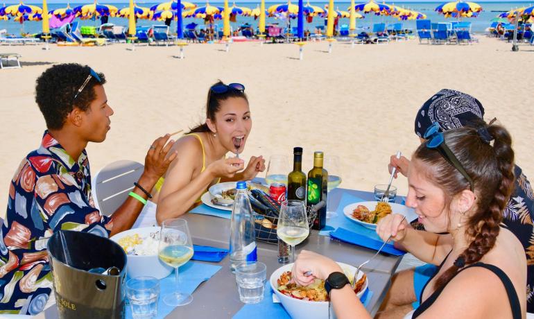 Vrienden lunchen op het strand onder kleurrijke parasols.