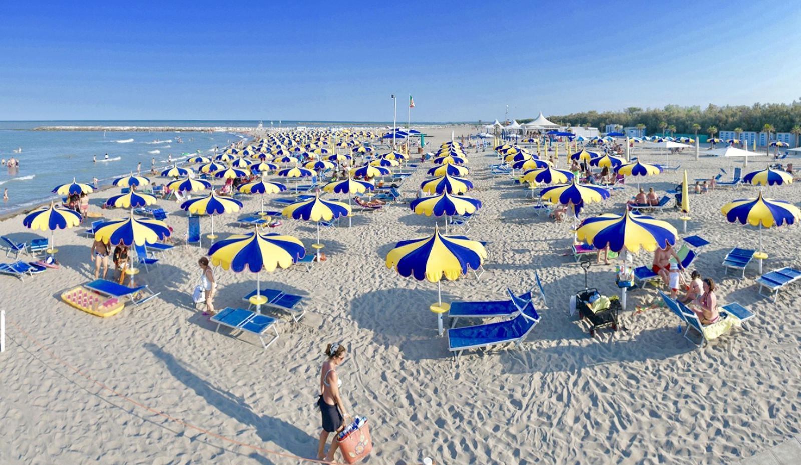 Spiaggia affollata con ombrelloni colorati, mare calmo e vegetazione rigogliosa sullo sfondo.