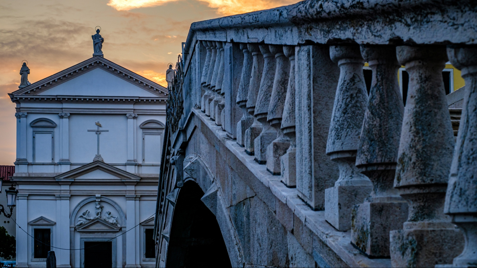 Ponte in pietra e chiesa al tramonto con cielo nuvoloso.