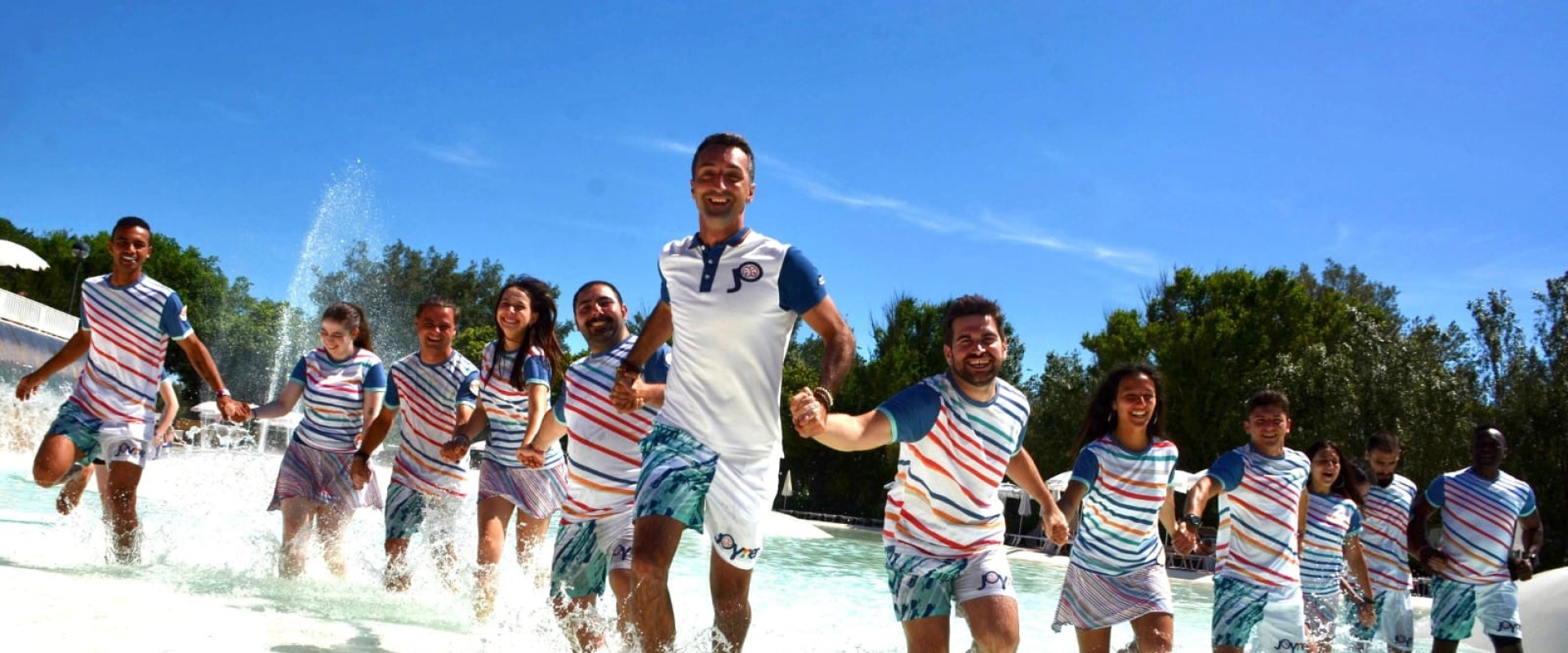 Persone in spiaggia festeggiano con una danza di gruppo, vestite in modo colorato.