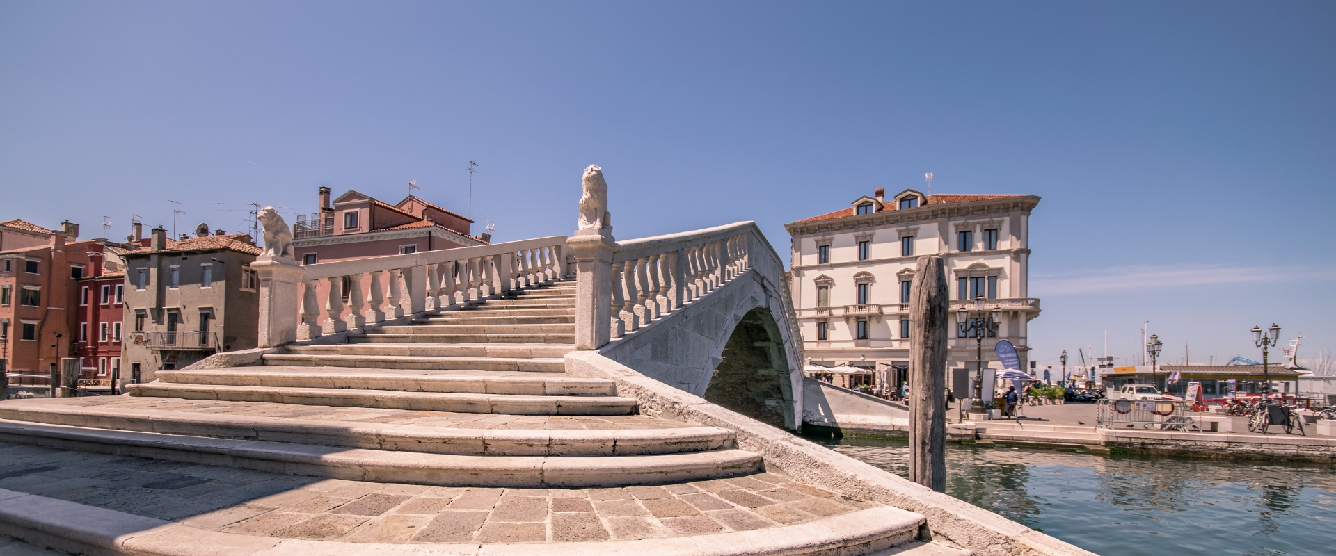 Ponte con statue di leoni, case storiche e canale in una città italiana.