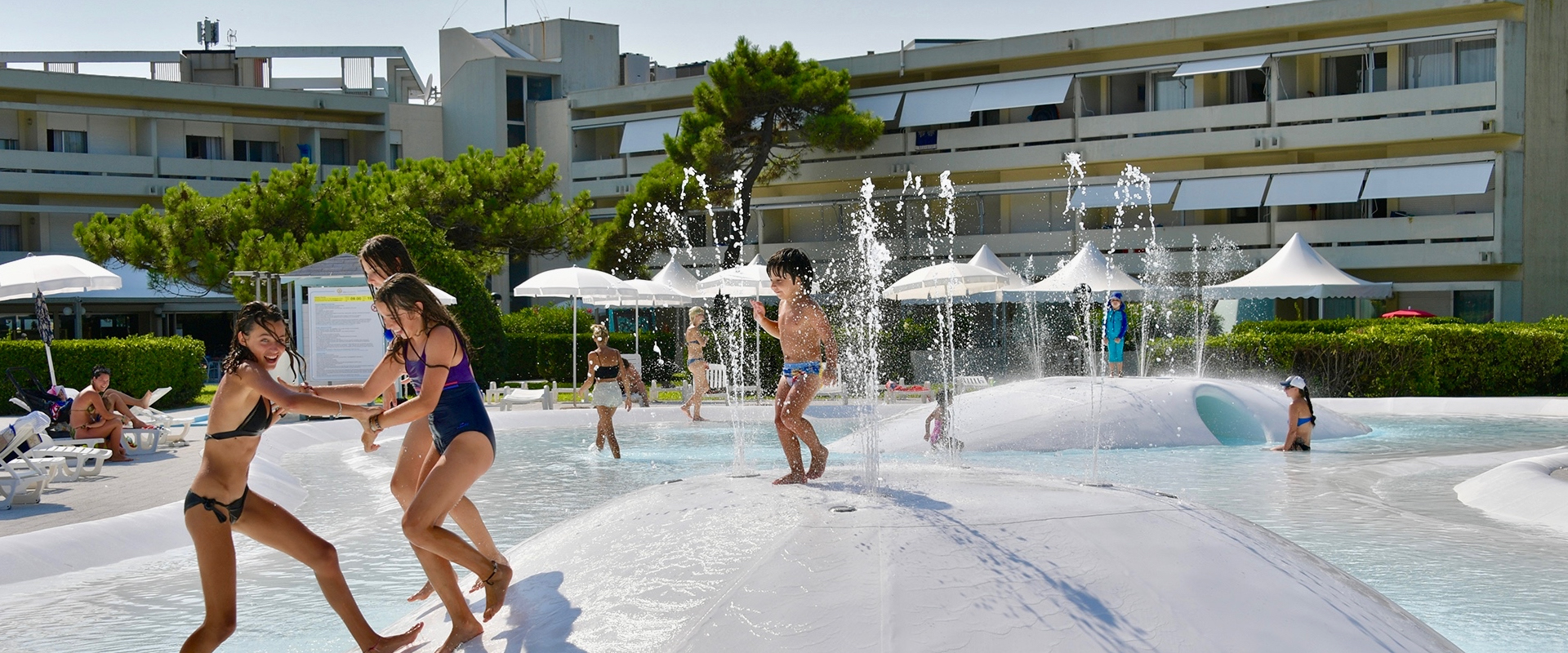 Complesso residenziale con piscina e giardini, circondato da verde e palazzi moderni.