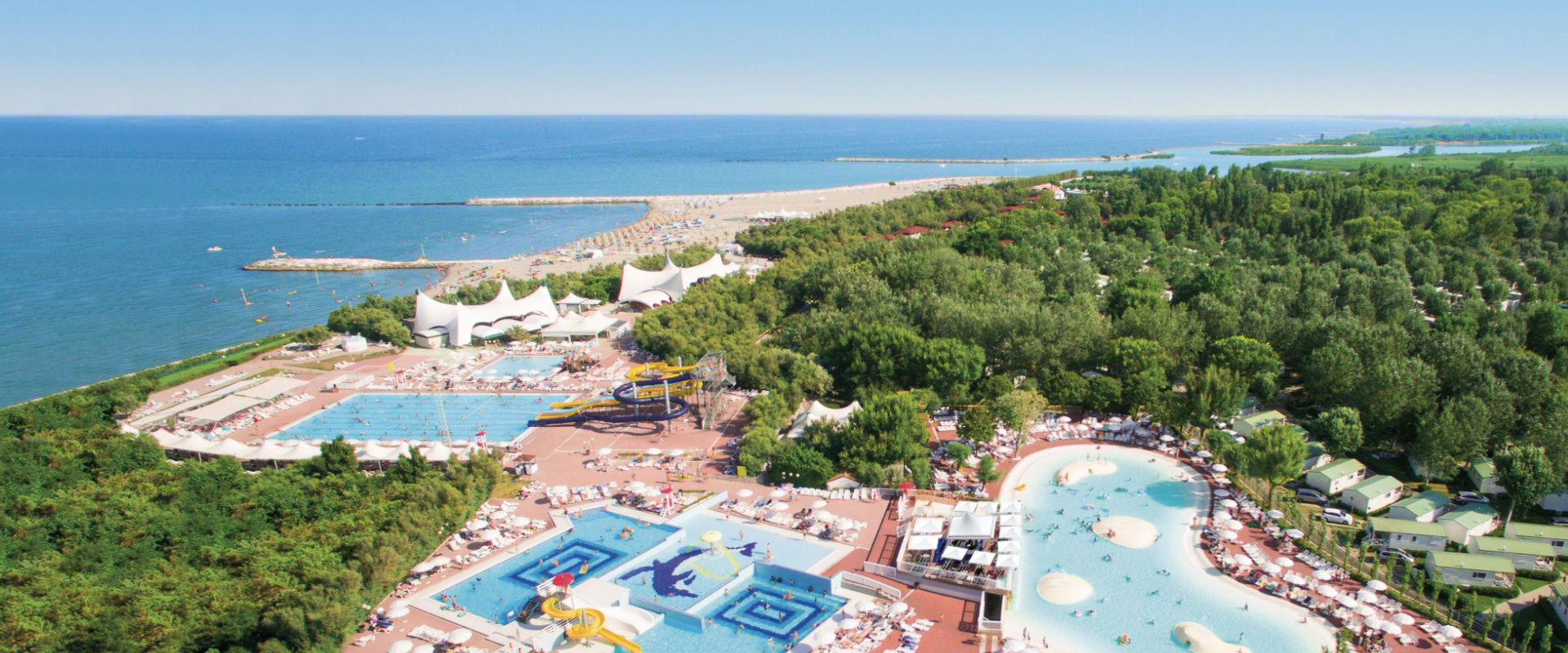 Villaggio turistico con piscine, scivoli e spiaggia immerso nel verde, fronte mare.