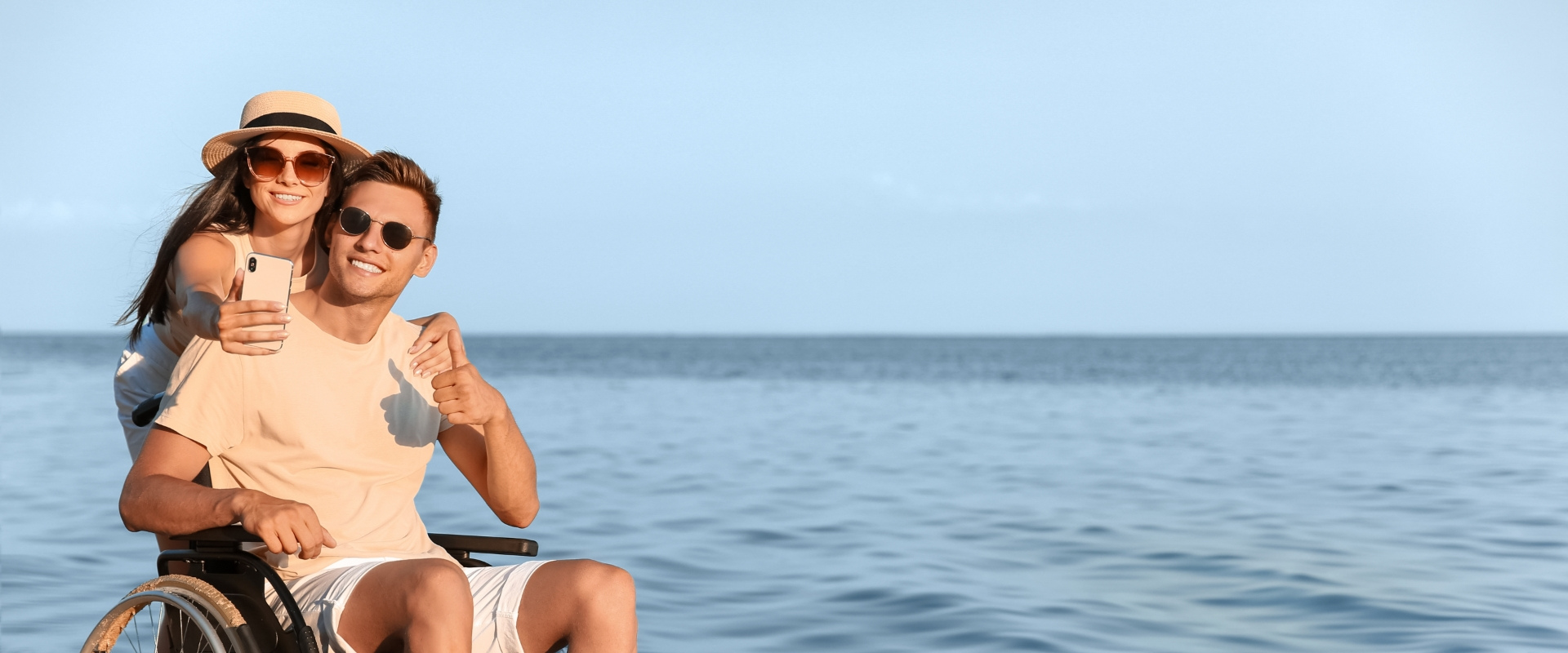 Coppia felice in spiaggia, lui in sedia a rotelle, scattando un selfie.