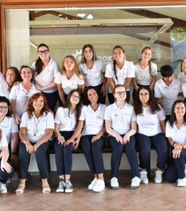 Gruppo di persone in uniforme bianca e pantaloni scuri, sorridenti davanti a un edificio.