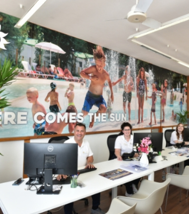 Ufficio moderno con personale sorridente e grande poster di bambini in piscina.