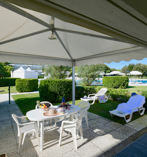 Terrazza con tavolo, sedie e vista piscina soleggiata.