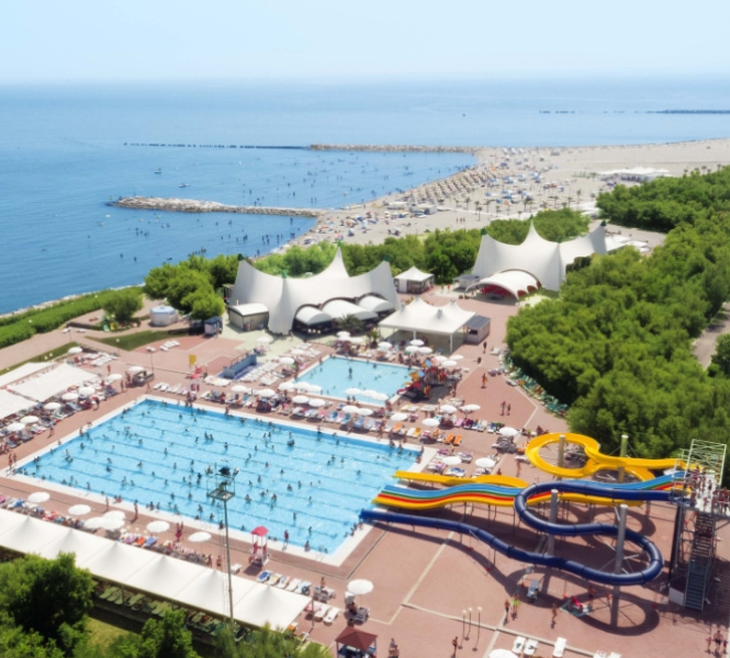 Parco acquatico con piscine, scivoli colorati e vista sul mare e spiaggia.