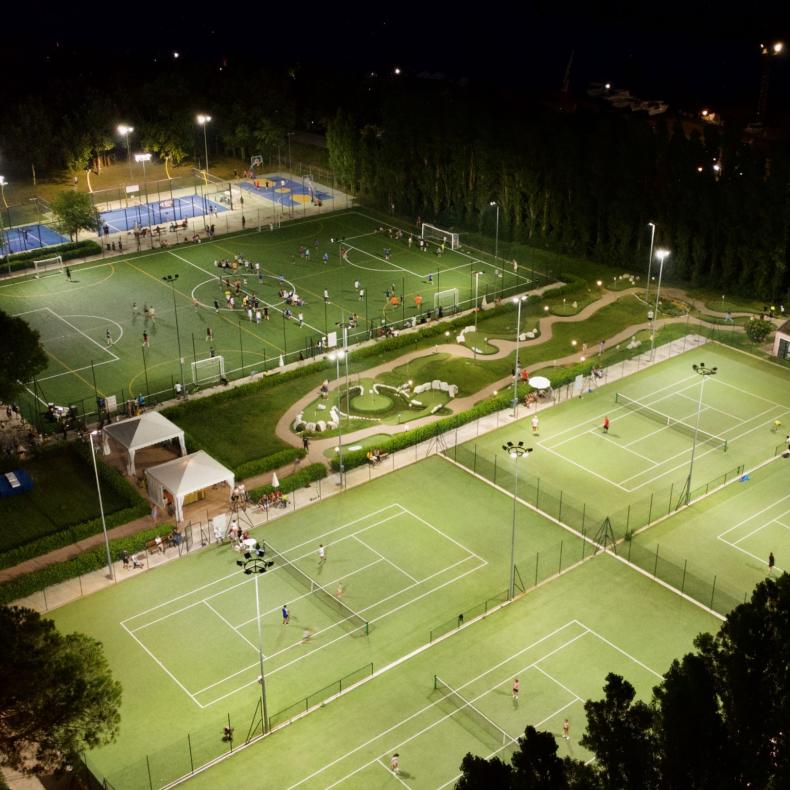 Giocatori di padel su un campo blu all'aperto, circondato da alberi e siepi.