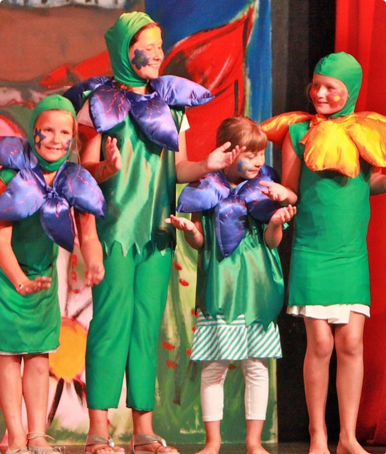 Bambini in costumi floreali verdi sul palco durante uno spettacolo teatrale.