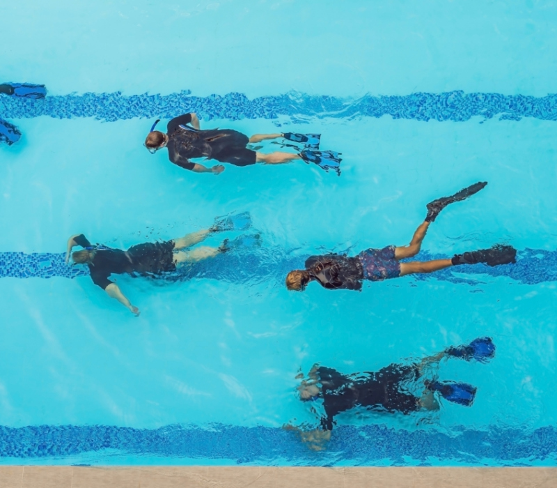 Persone nuotano in piscina con pinne e maschere, viste dall'alto.