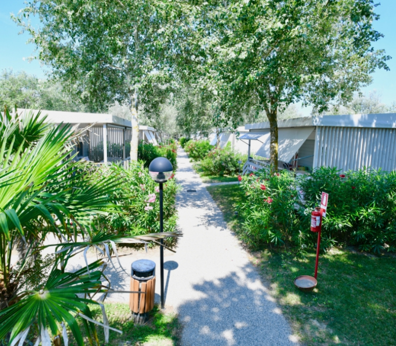 Sentiero tra bungalow immersi nella vegetazione, con lampioni e estintore visibili.