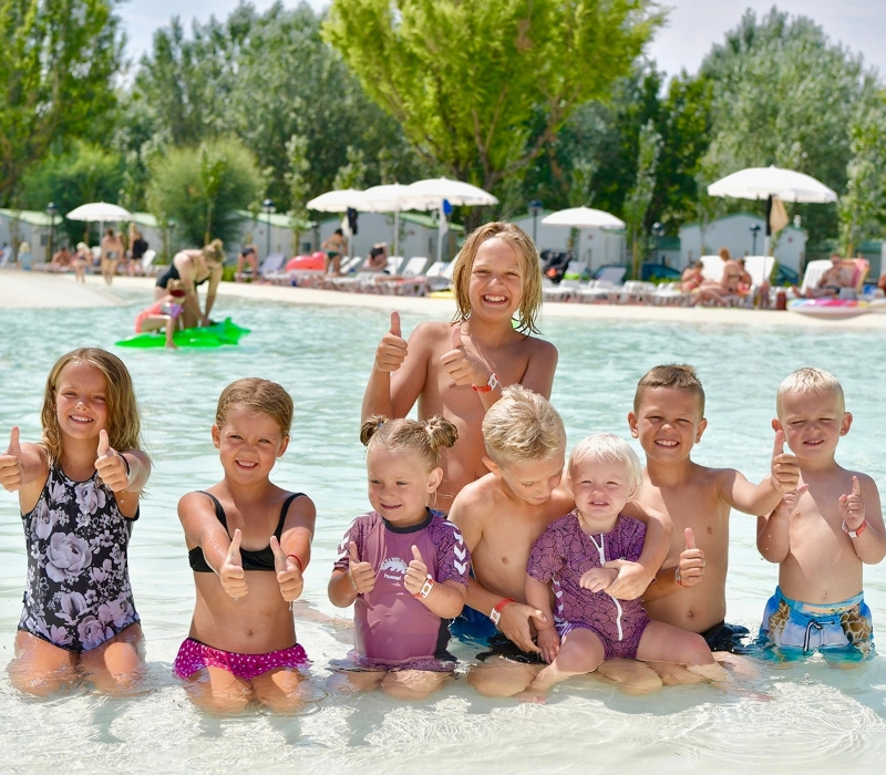 Bambini sorridenti in piscina, con pollici in su, in una giornata di sole.