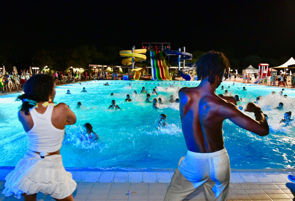 Festa notturna in piscina con musica, balli e scivoli colorati.