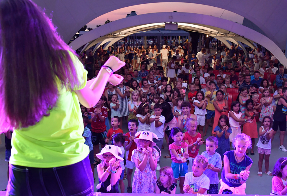 Bambini partecipano a un evento con una folla sotto un'ampia struttura coperta.