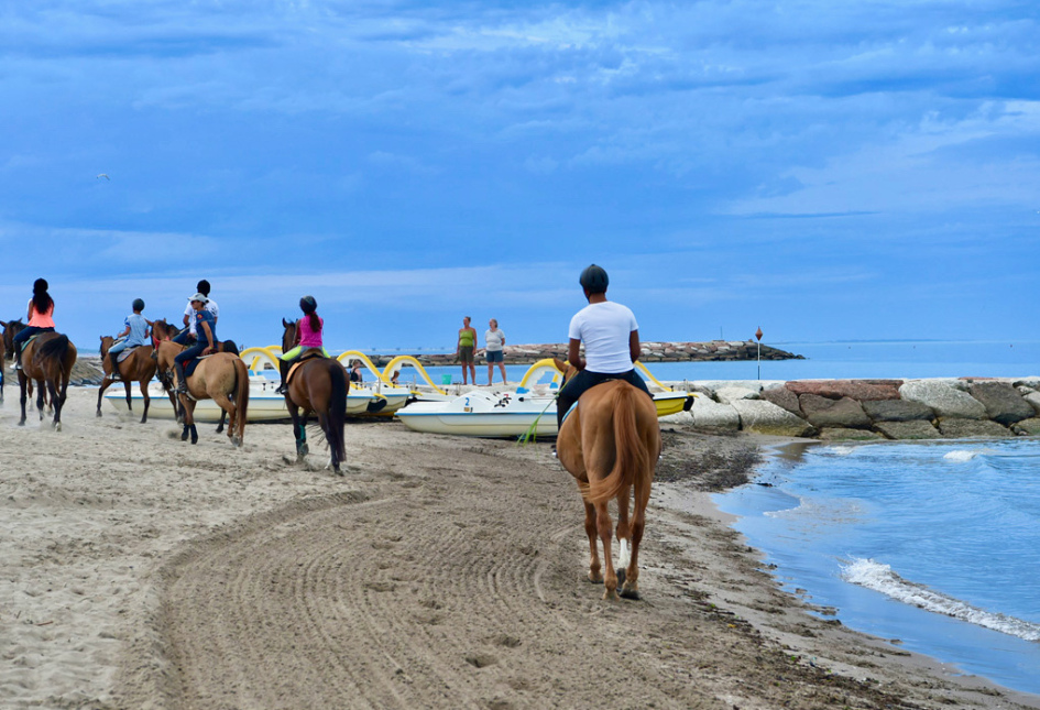 Cavalieri a cavallo lungo la spiaggia, vicino al mare e pedalò gialli.