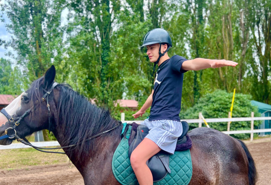 Persona su cavallo con casco e braccia aperte in una giornata all'aperto.