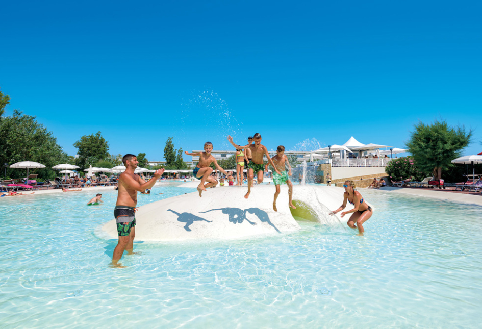 Famiglia si diverte in piscina con giochi d'acqua sotto il sole estivo.