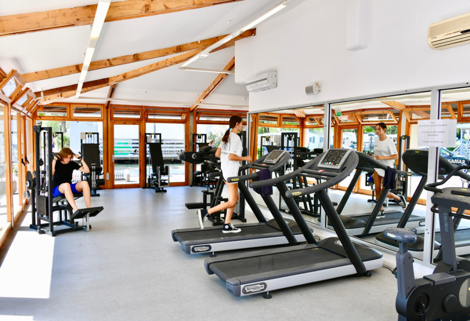 Palestra luminosa con persone che si allenano su tapis roulant e attrezzi.