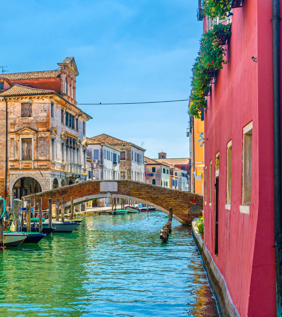 Canale con ponte in mattoni, edifici colorati e cielo sereno.