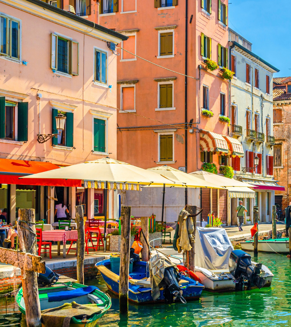 Colorati edifici e barche lungo un canale con tavoli all'aperto.